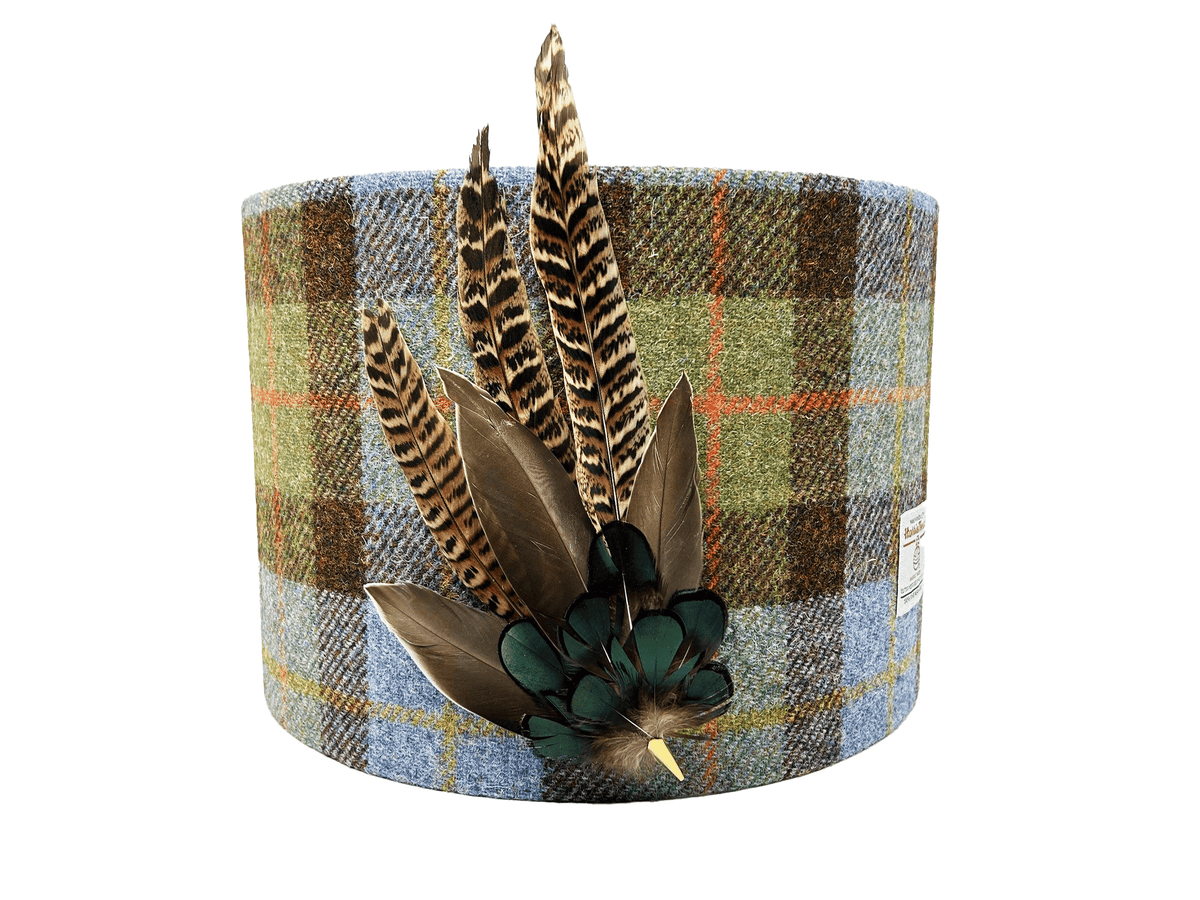 A cylindrical lampshade made of Harris Tweed with a plaid pattern and decorated with real pheasant feathers attached to the top.