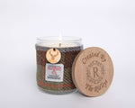 A glass soy wax candle with a whisky fragrance, adorned with a Harris Tweed sleeve and a wooden lid featuring Created By The Ridleys logo